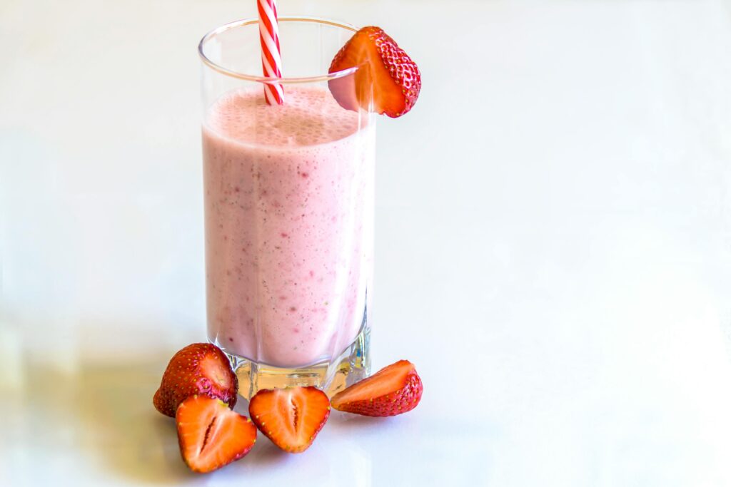 pexels-photo-103566-103566 Delicious strawberry smoothie in a glass with fresh strawberries and a striped straw on a light background.