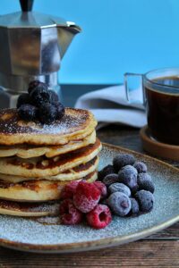 Stack of pancakes with berries and coffee, perfect for a cozy breakfast.