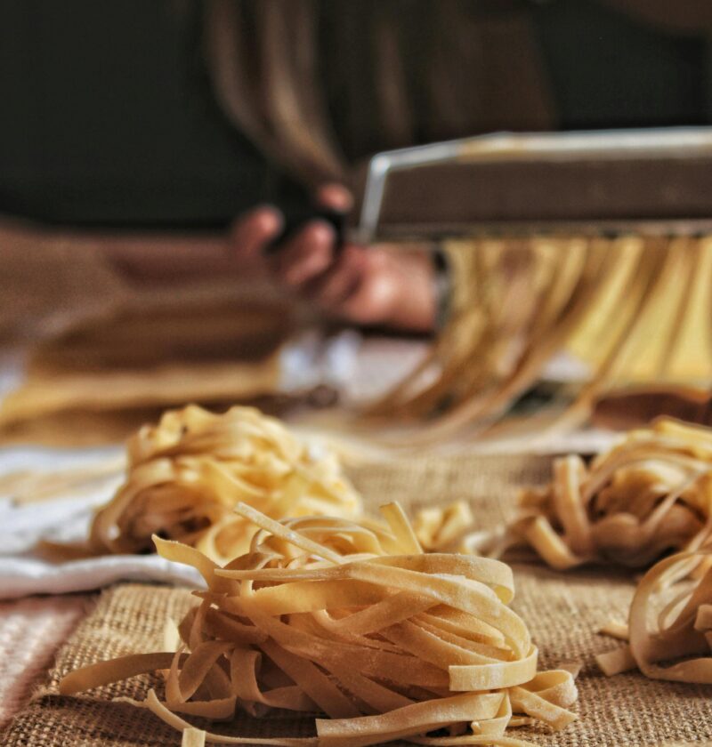 Close-up of handcrafted pasta being made with a pasta machine, showcasing the artisanal process indoors.