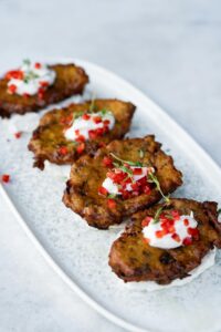 Delicious zucchini fritters with cream and red pepper on a white platter.