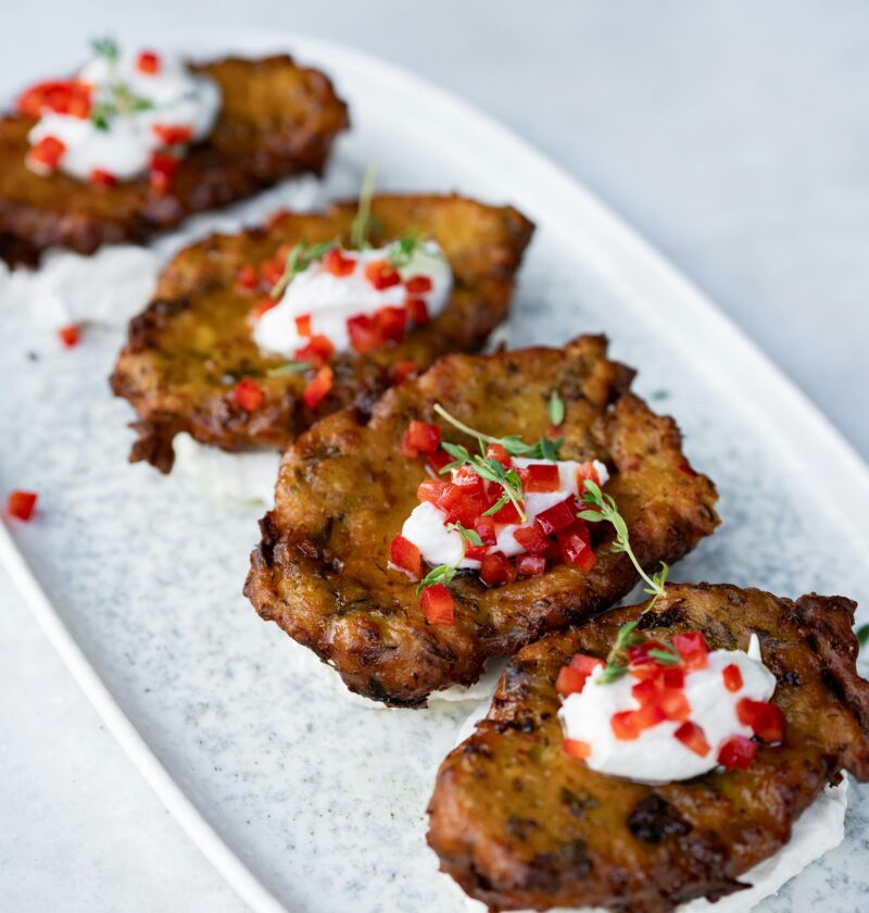 Delicious zucchini fritters with cream and red pepper on a white platter.