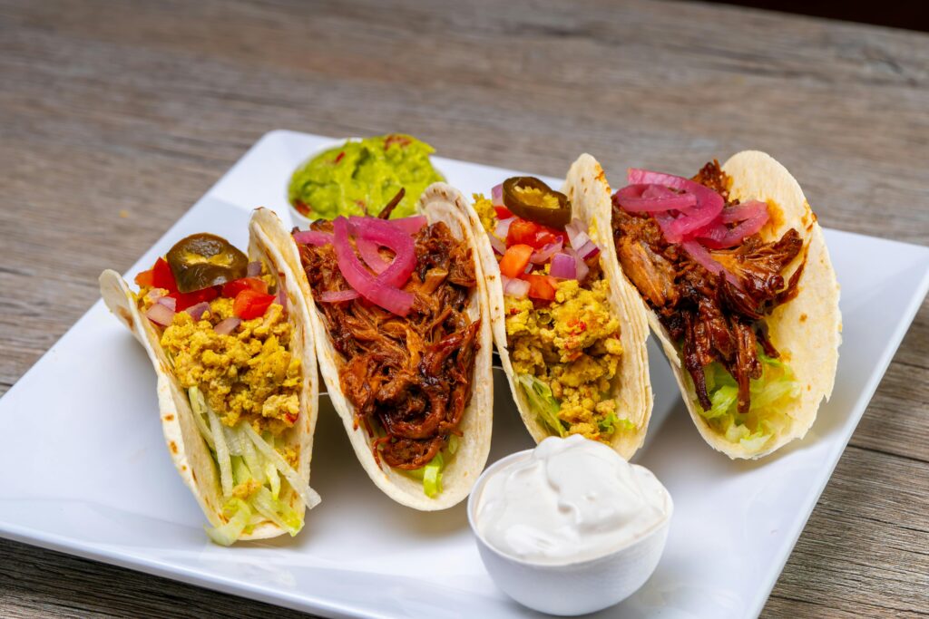 Tasty tacos filled with meat and vegetables served on a plate with sauces.