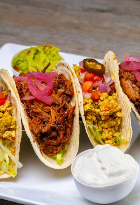Tasty tacos filled with meat and vegetables served on a plate with sauces.