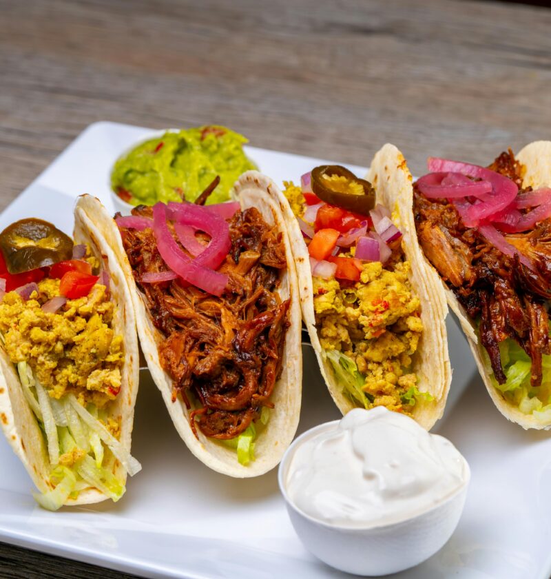 Tasty tacos filled with meat and vegetables served on a plate with sauces.