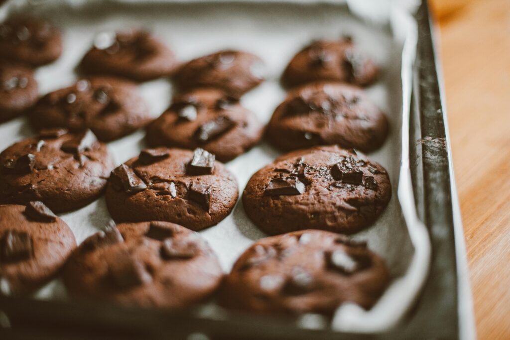 pexels-photo-5847099-5847099 Close-up of freshly baked chocolate cookies with chocolate chunks on a baking tray.