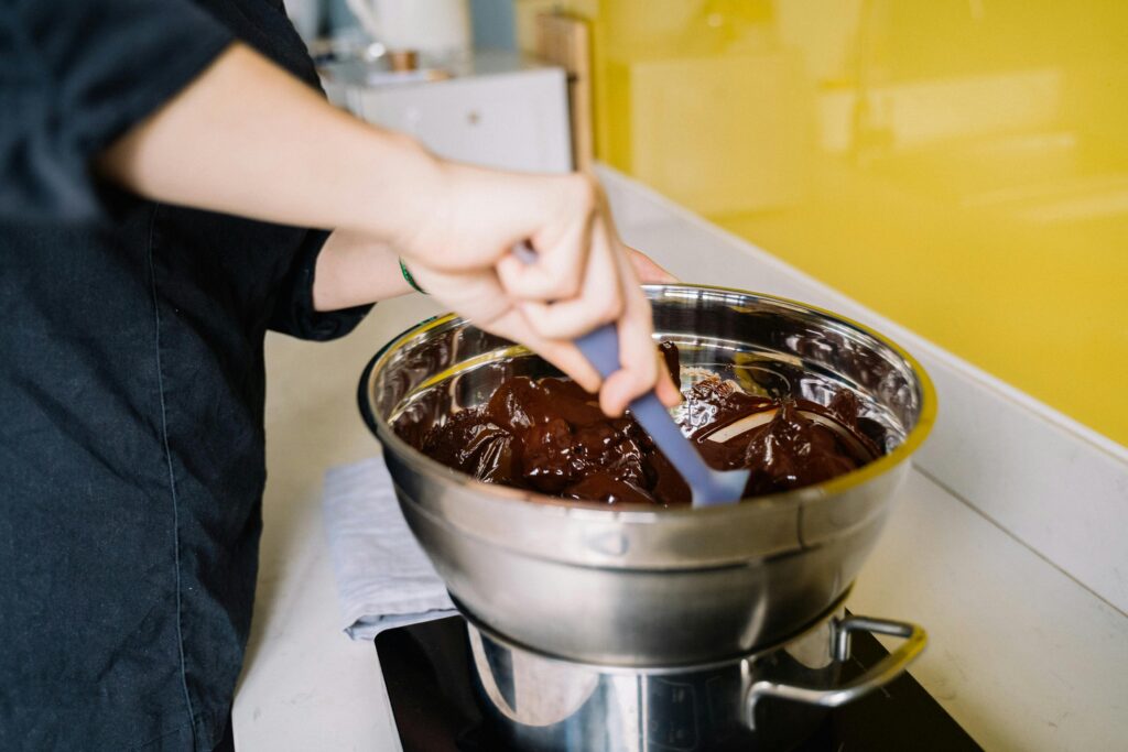 pexels-photo-6035317-6035317 A person mixes rich melted chocolate in a stainless steel bowl for dessert preparation.