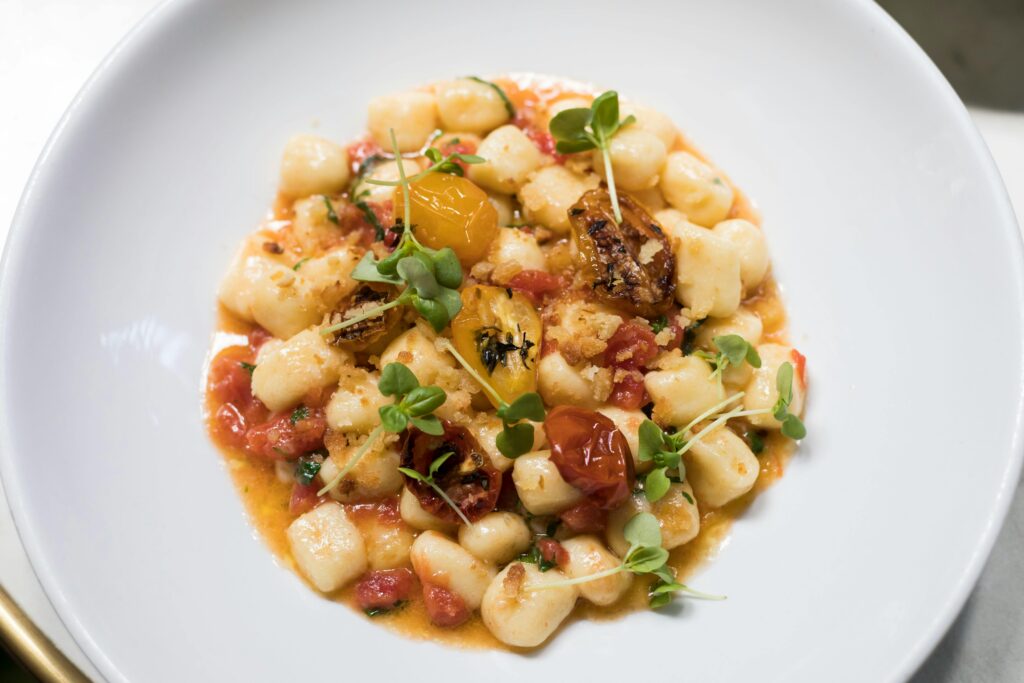Top view of homemade gnocchi with fresh tomatoes and herbs on a white plate.
