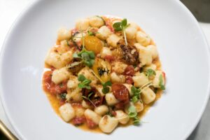 Top view of homemade gnocchi with fresh tomatoes and herbs on a white plate.