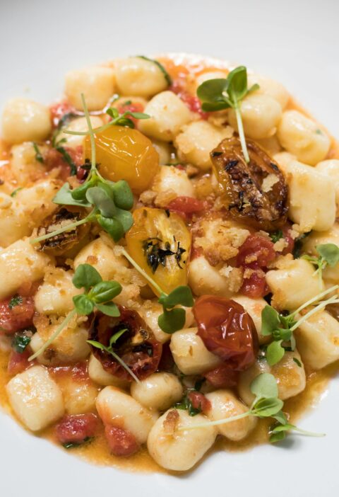 Top view of homemade gnocchi with fresh tomatoes and herbs on a white plate.