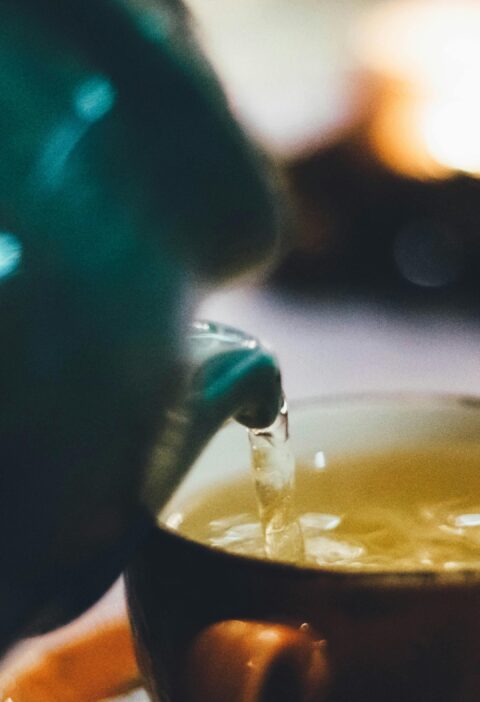 Warm close-up image of tea being poured into a teacup with blurred background ambiance.