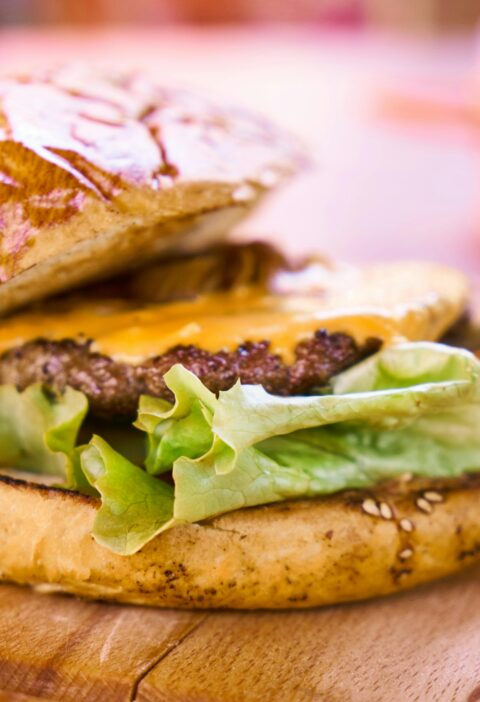 Close-up of a delicious cheeseburger with melted cheese and fresh lettuce on a wooden surface.