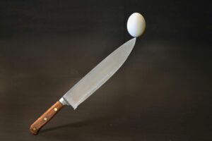 A striking image of a knife skillfully balancing an egg against a dark backdrop, showcasing precision.