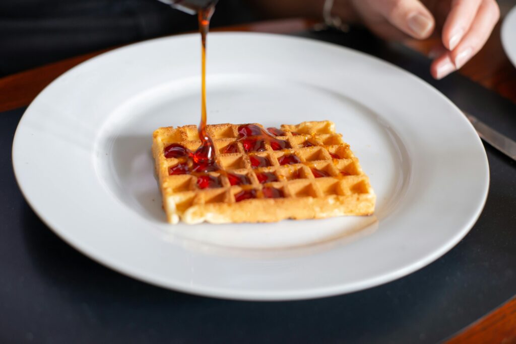 Close-up of a waffle being drizzled with syrup on a white plate, Portugal.