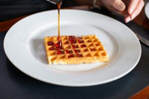 Close-up of a waffle being drizzled with syrup on a white plate, Portugal.