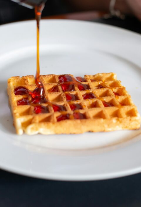 Close-up of a waffle being drizzled with syrup on a white plate, Portugal.