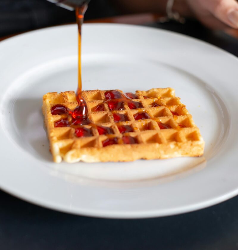 Close-up of a waffle being drizzled with syrup on a white plate, Portugal.