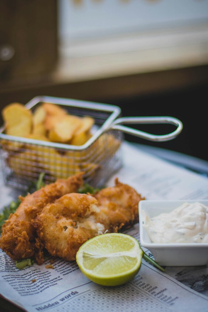 pexels-photo-1123249-1123249 Close-up of crispy fish and chips with tartar sauce and lime on newspaper.