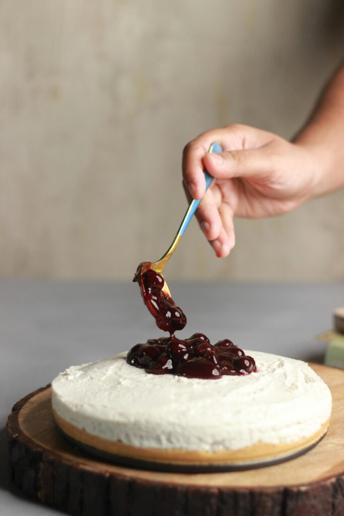 Cherry topping being spooned onto a creamy cheesecake for a sweet treat.