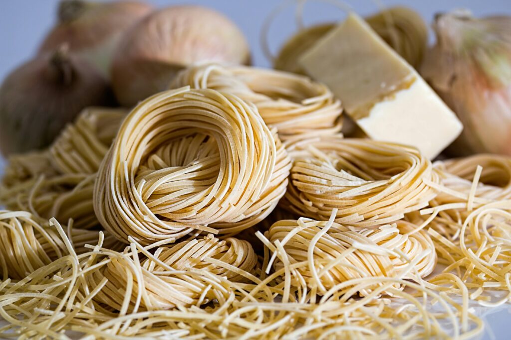 A close-up view of uncooked capellini pasta nests surrounded by onions and cheese.