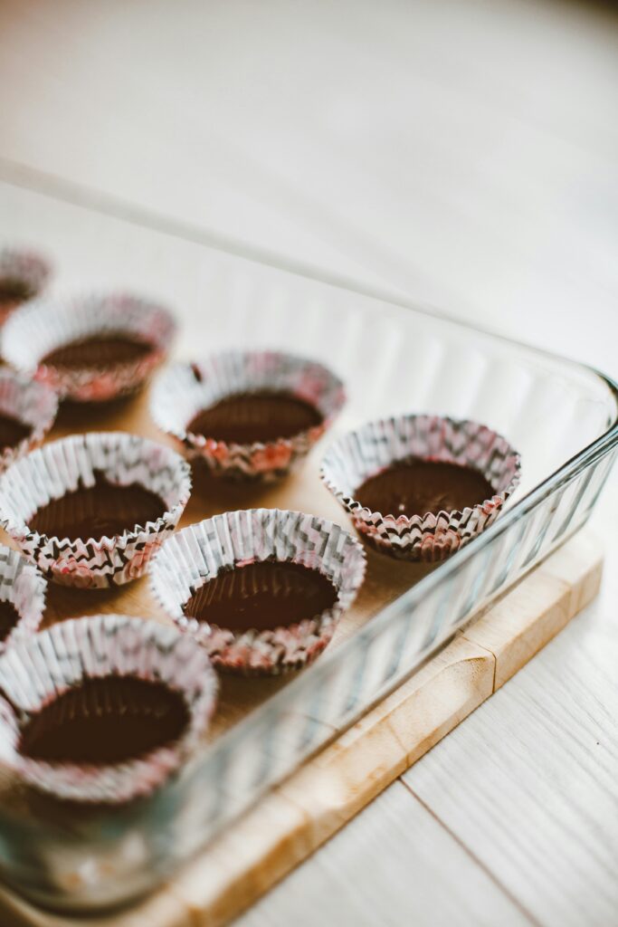 Glass baking tray with chocolate muffin batter in paper cups, ready to bake.