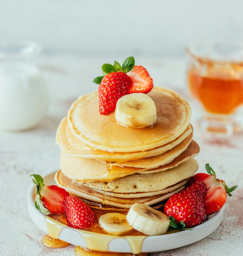 Stack of fluffy pancakes with strawberries, banana, and syrup.