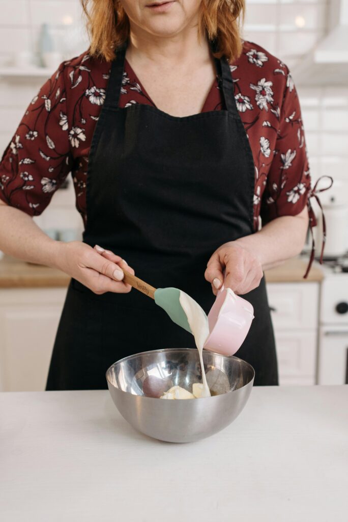A woman in an apron pours liquid into a bowl, preparing dough in a stylish kitchen.