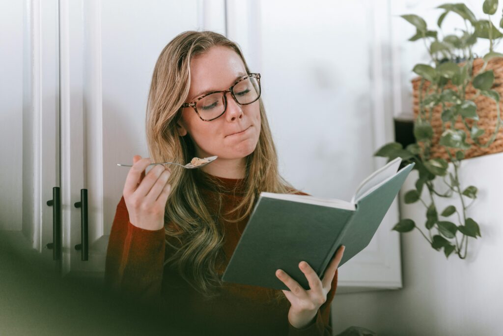 Woman enjoying a quiet moment reading a book and eating yogurt in her cozy home.