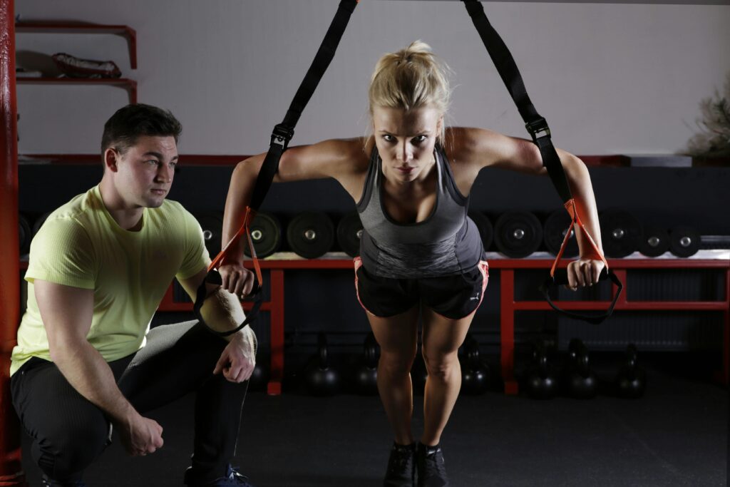 pexels-photo-414029-414029 A woman performing strength training with a trainer in a gym setting, showcasing fitness and dedication.