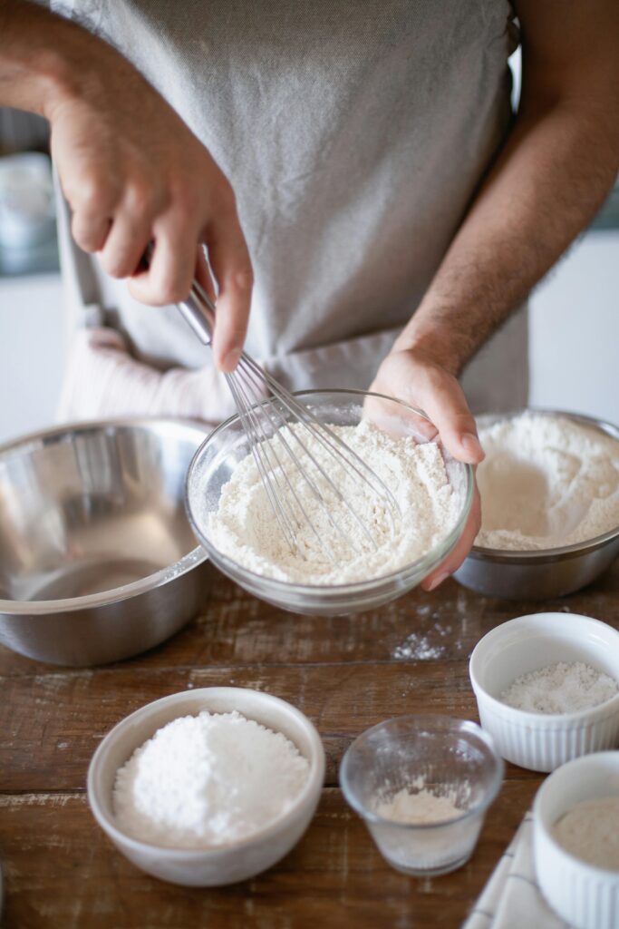 pexels photo 8477750 8477750 A baker whisks flour in a bowl amidst other ingredients, ready for baking.