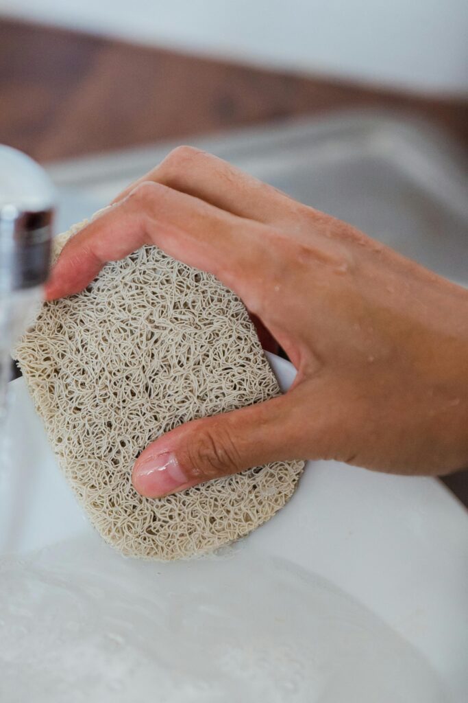 Detailed view of a hand scrubbing a dish with a textured sponge in a kitchen setting.